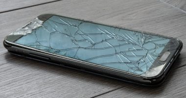 Broken smartphone on the floor. The screen is cracked and the phone is damaged.